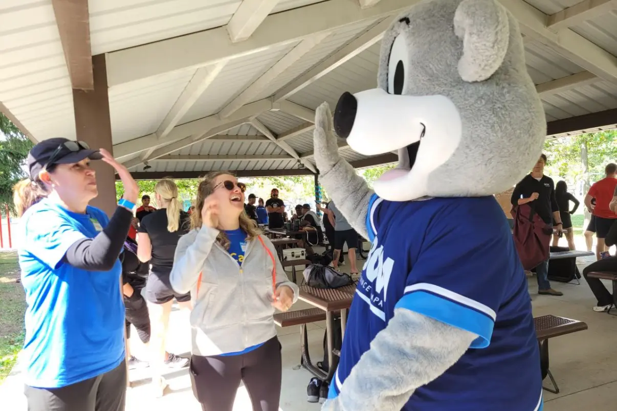 BCM mascot Bertie high-fiving a laughing woman at an outdoor park event