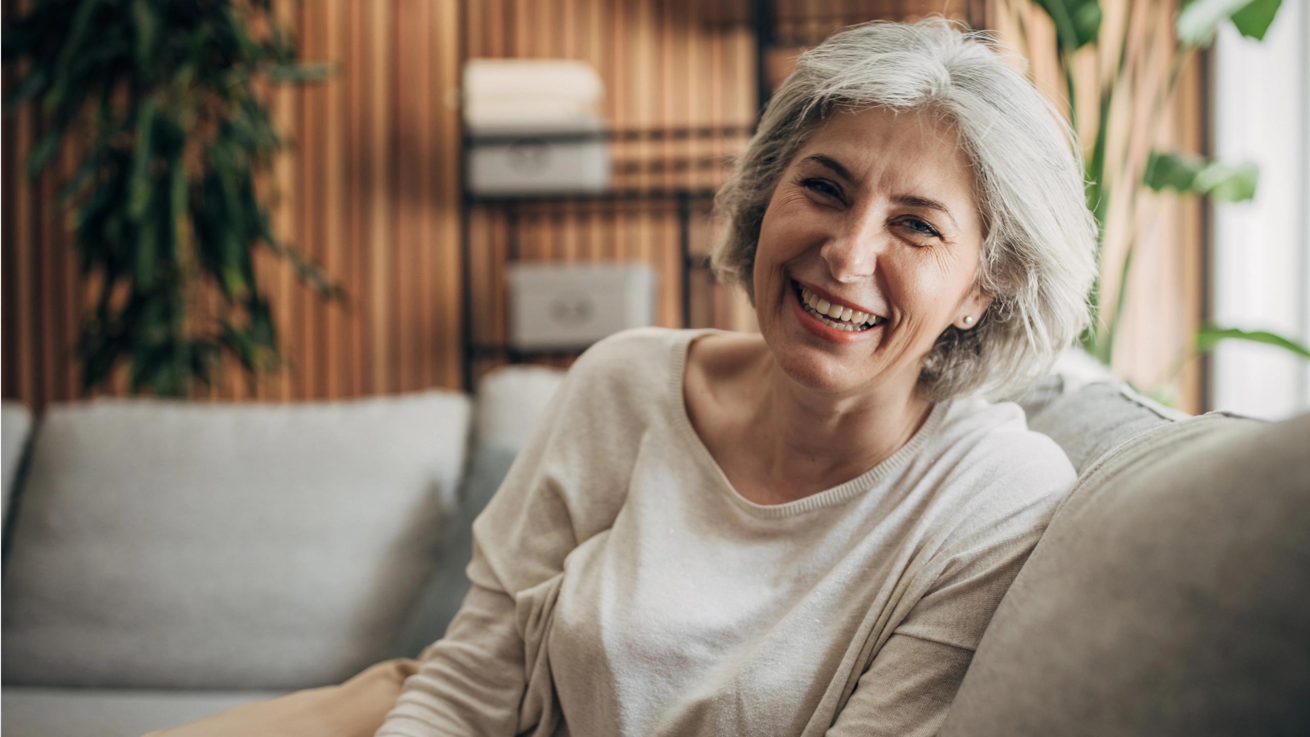 A woman with short grey hair laughing, sitting in the living room of her home