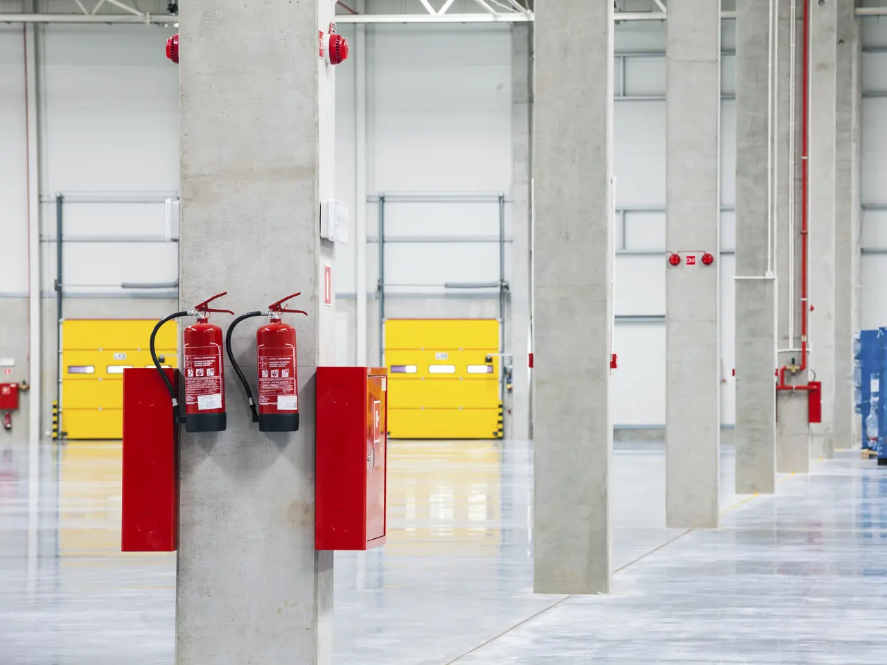 Fire extinguishers and hose cabinets mounted on a concrete column in a warehouse